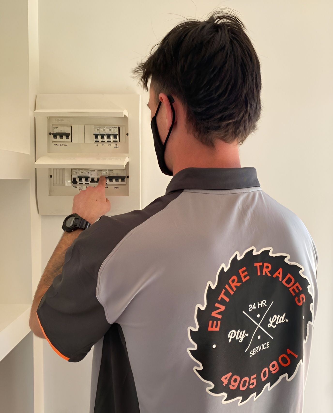 Technician in a gray shirt inspecting an electrical panel indoors for Electrician Newcastle services
