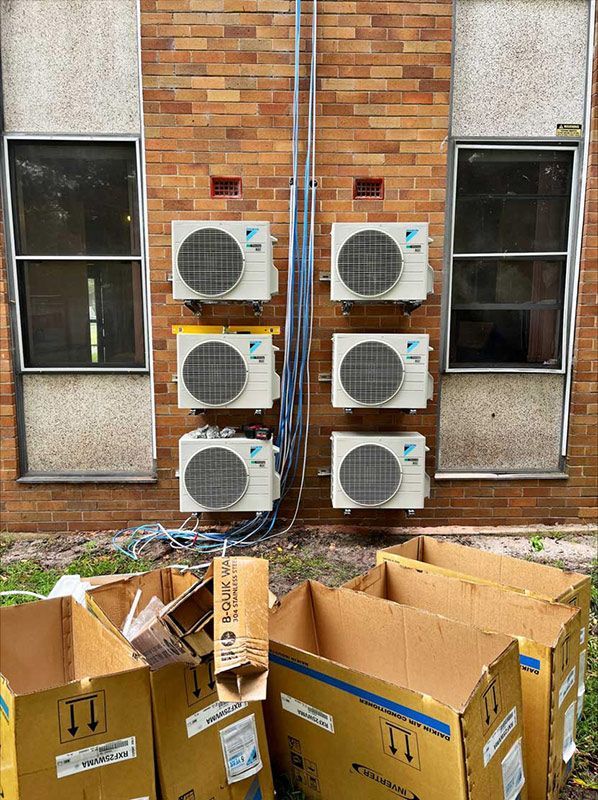 A Row Of Six Air Conditioners Are Mounted On The Side Of A Brick Building — Entire Trades in Port Stephens, NSW
