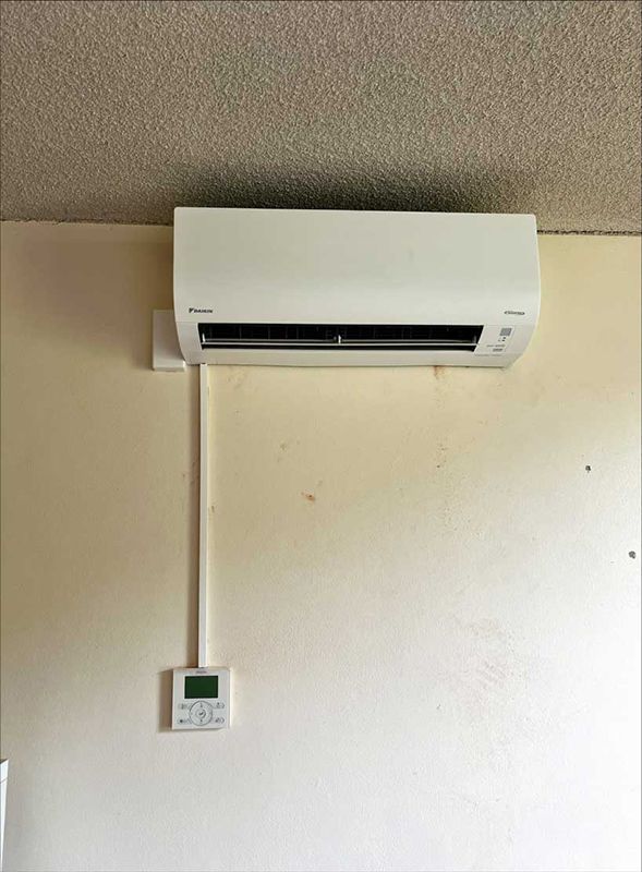 A White Air Conditioner Is Mounted On A Wall Next To A Remote Control — Entire Trades in Port Stephens, NSW