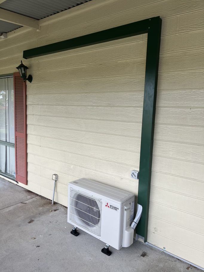 A White Air Conditioner Is Sitting on The Side of A House — Entire Trades in Maitland, NSW