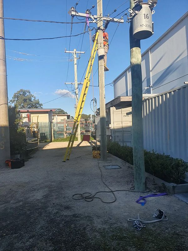 A Man On A Yellow Ladder Is Working On A Power Line — Entire Trades in Singleton, NSW