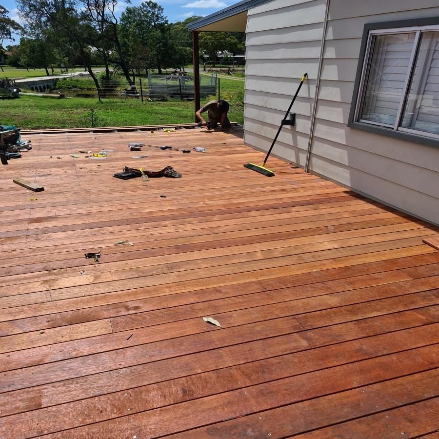 A Man Is Working on A Wooden Deck in Front of A House — Entire Trades in Maitland, NSW