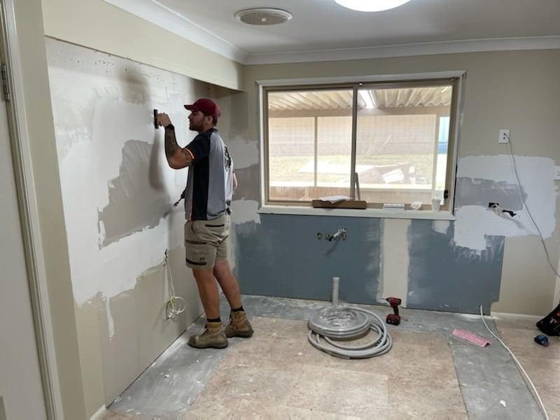 A Man Is Standing in A Room Painting a Wall — Entire Trades in Maitland, NSW