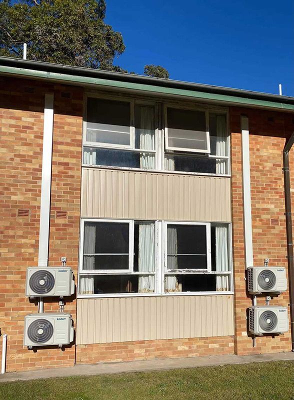 A Brick Building Wall With Four Air Conditioning Units — Entire Trades in Cessnock, NSW