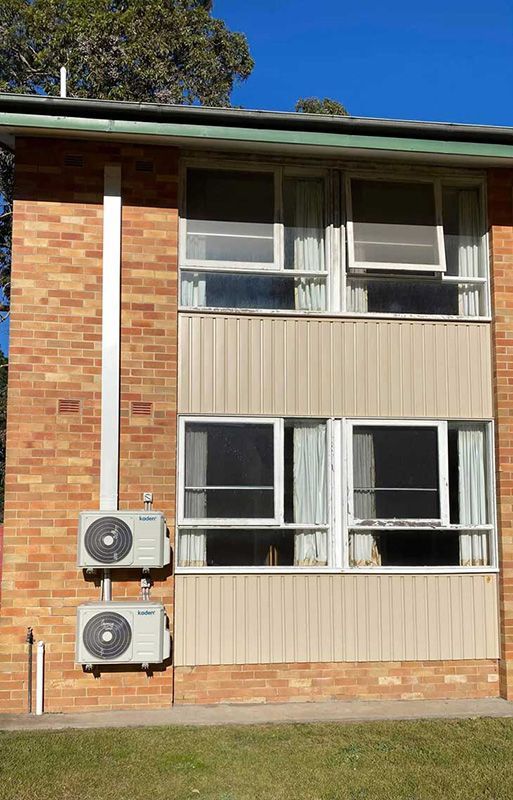 Exterior View Of A Brick Wall Building With Two Air Conditioners Installed On It — Entire Trades in Cessnock, NSW