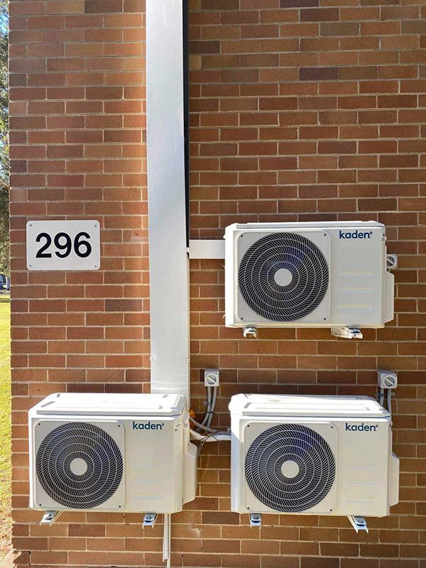 Three Air Conditioners Are Mounted On The Side Of A Brick Building With 296 Number Plate Hanging On It — Entire Trades in Cessnock, NSW