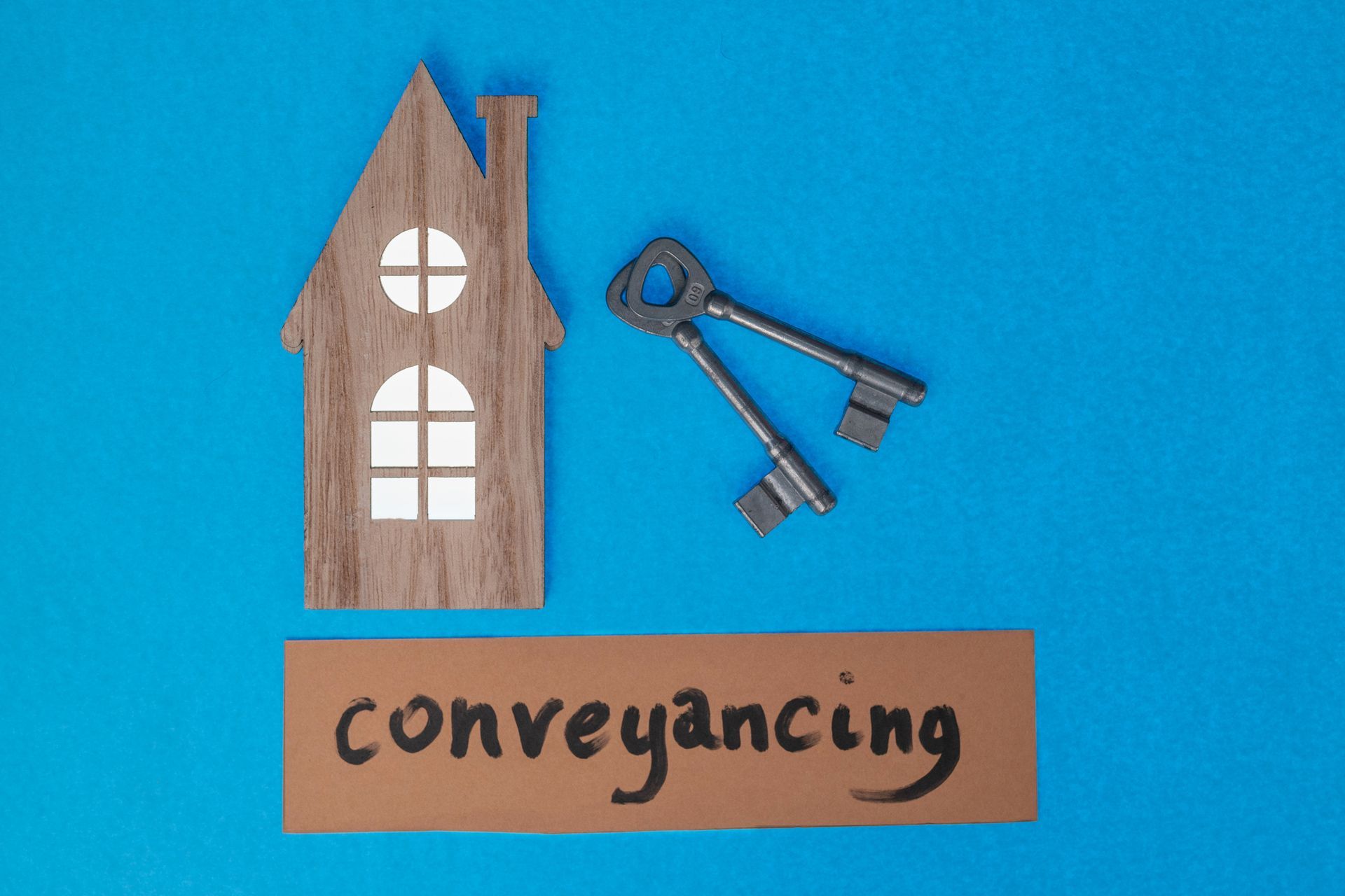 Wooden house and keys on blue background symbolizing property conveyancing process. Wooden house and keys on blue background symbolizing property conveyancing process.