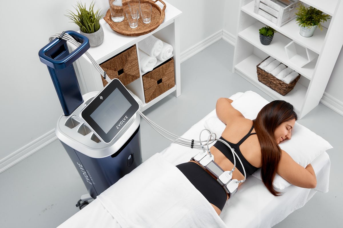 A woman is laying on a bed with a machine on her back.