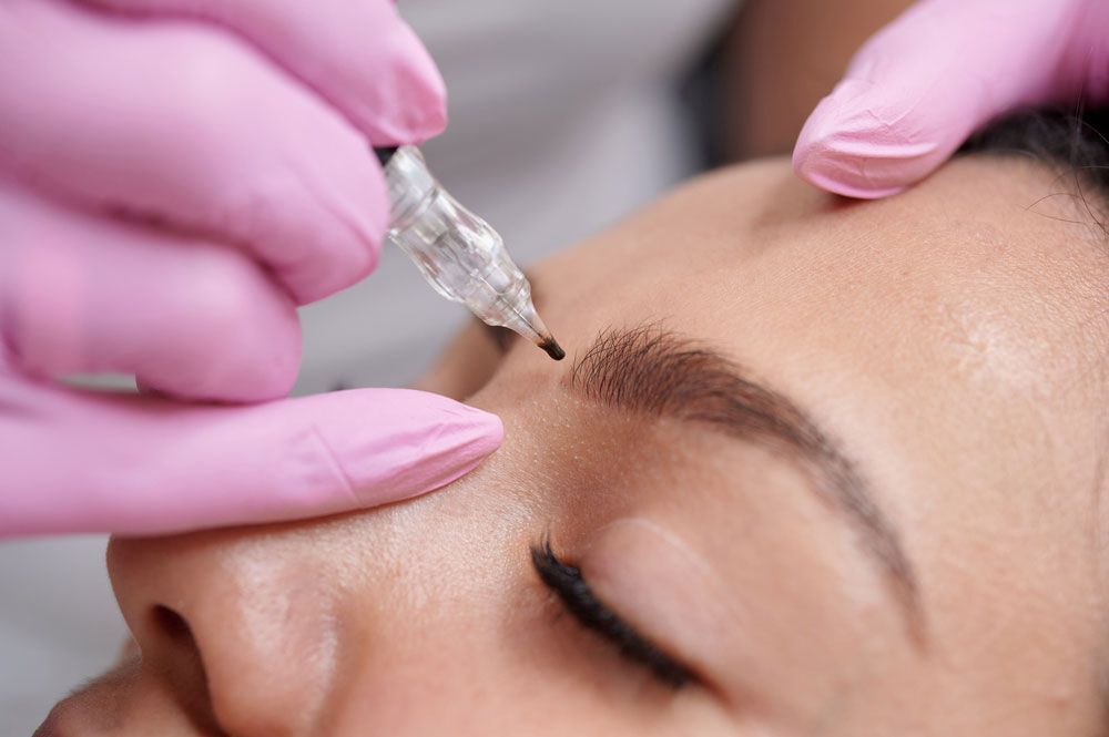 A woman is getting a permanent makeup tattoo on her eyebrows.