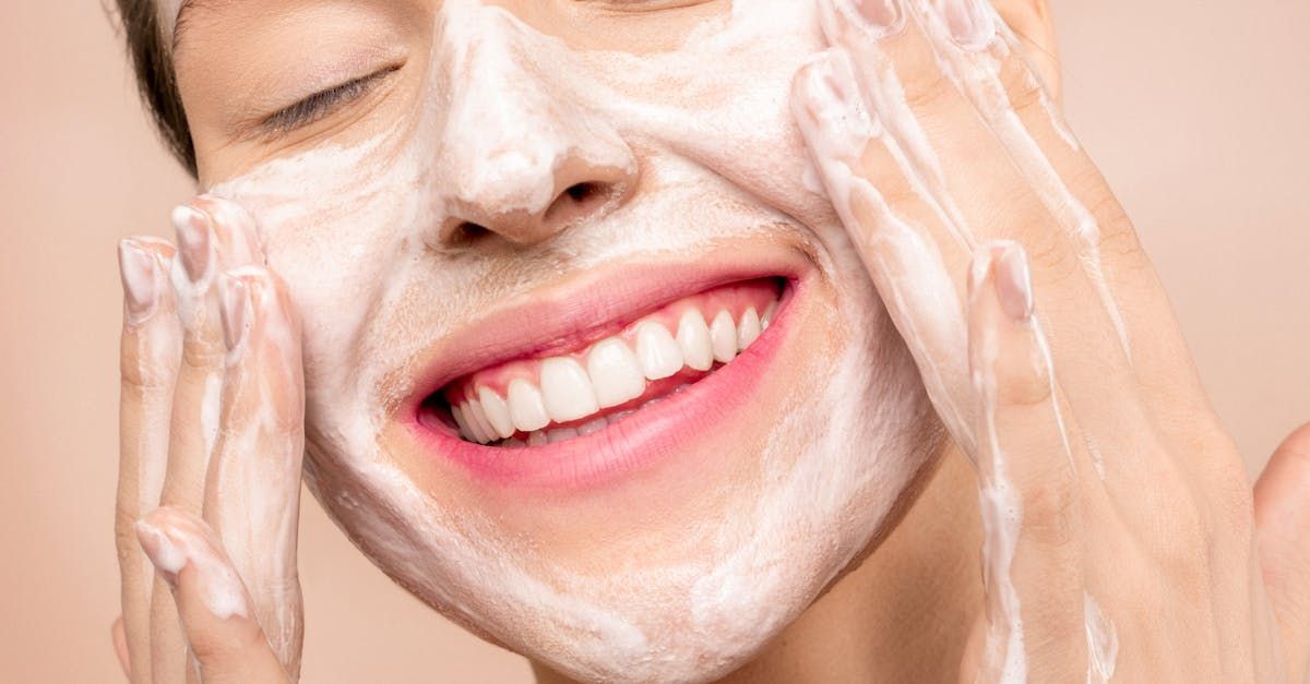 A woman is smiling while washing her face with soap.