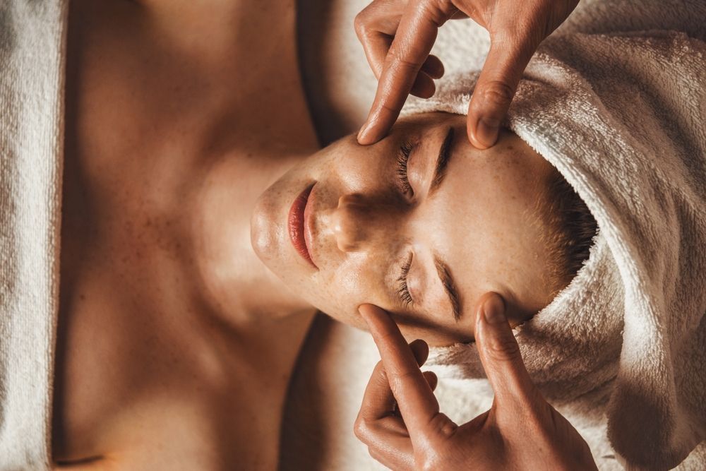 A woman with a towel wrapped around her head is getting a facial massage.