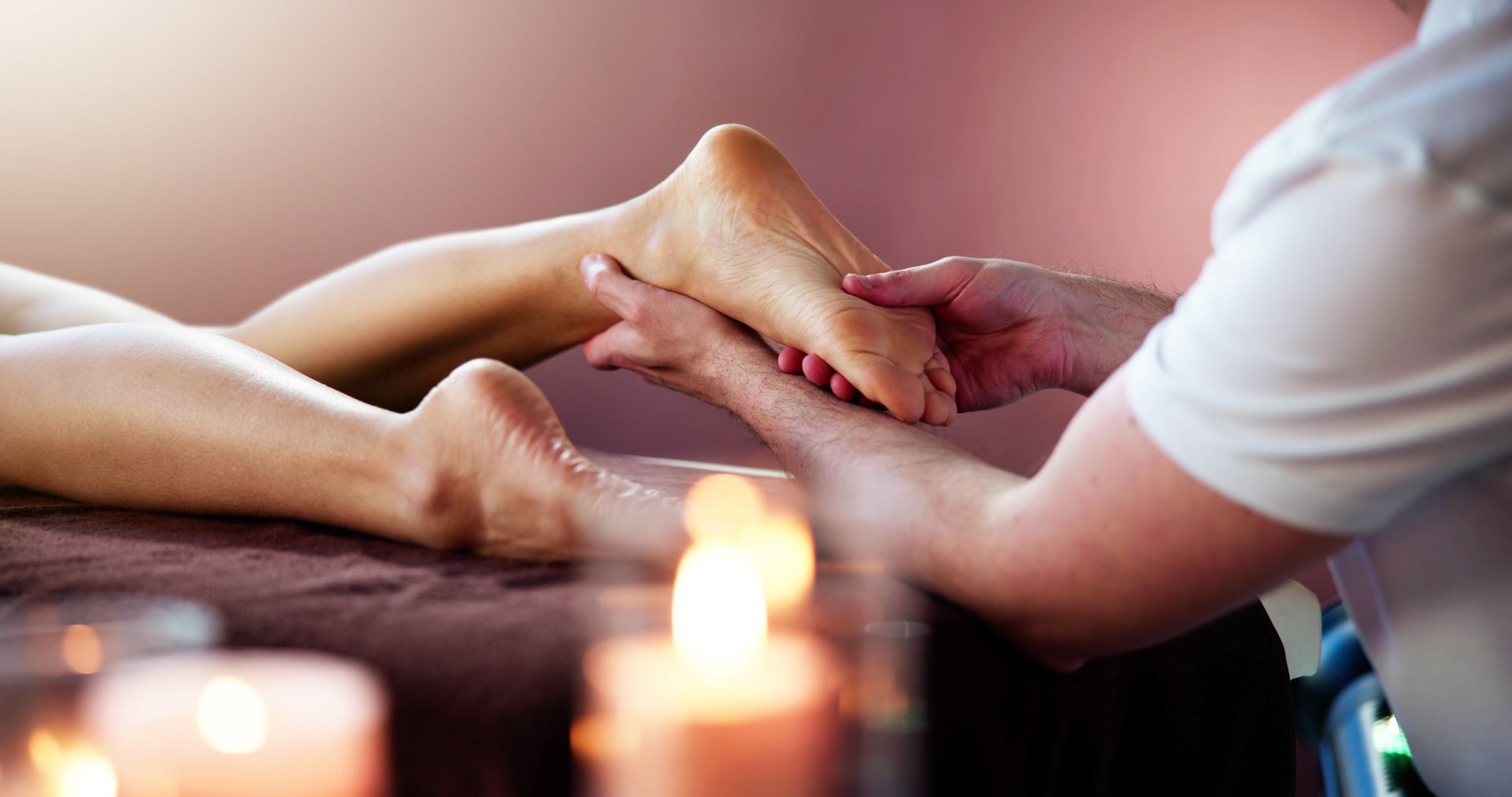 A woman is getting a foot massage in a spa with candles in the background.