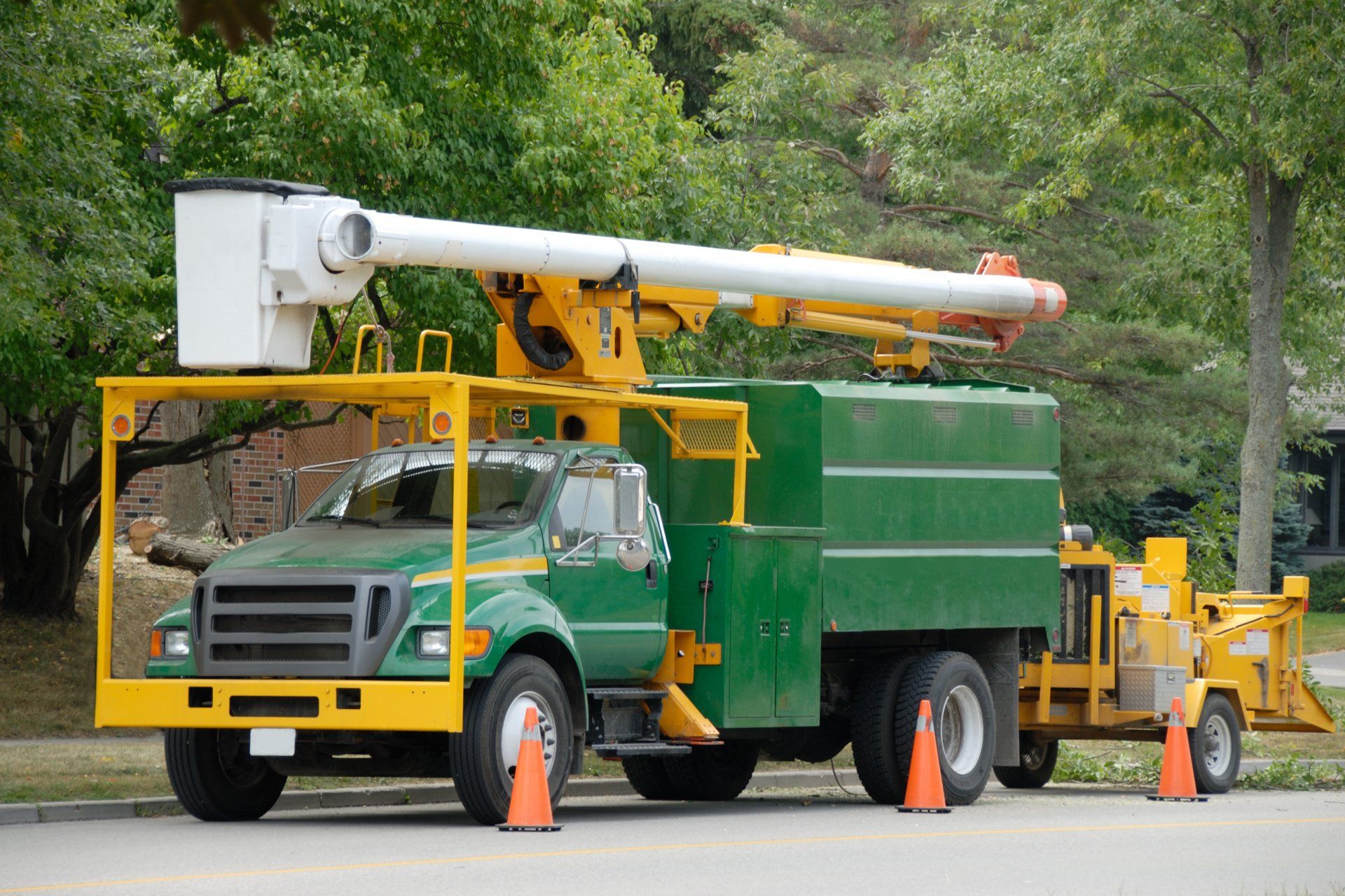 A green and yellow tree trimming truck is parked on the side of the road.