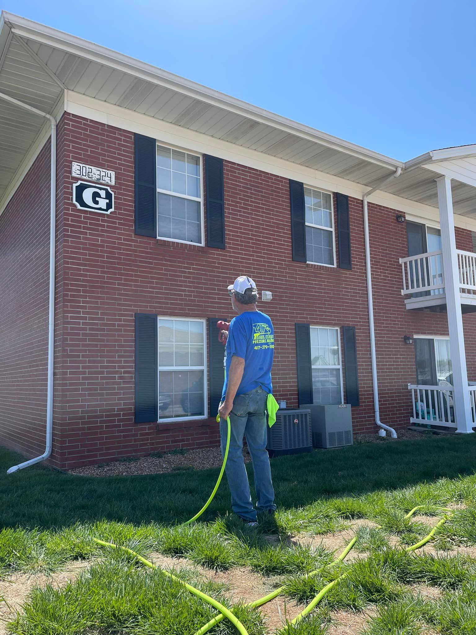 A man is spraying a lawn with a hose in front of a brick building.