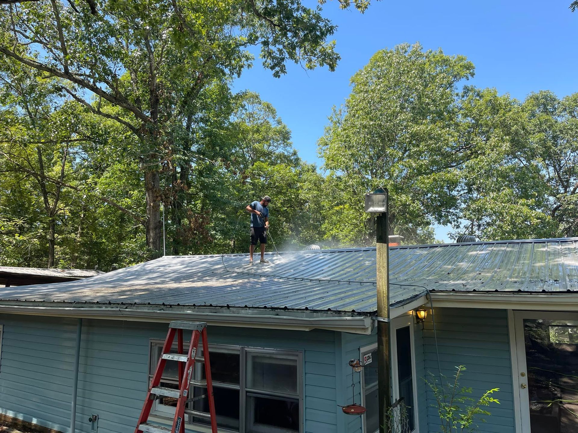 A man is cleaning the roof of a house with a pressure washer.