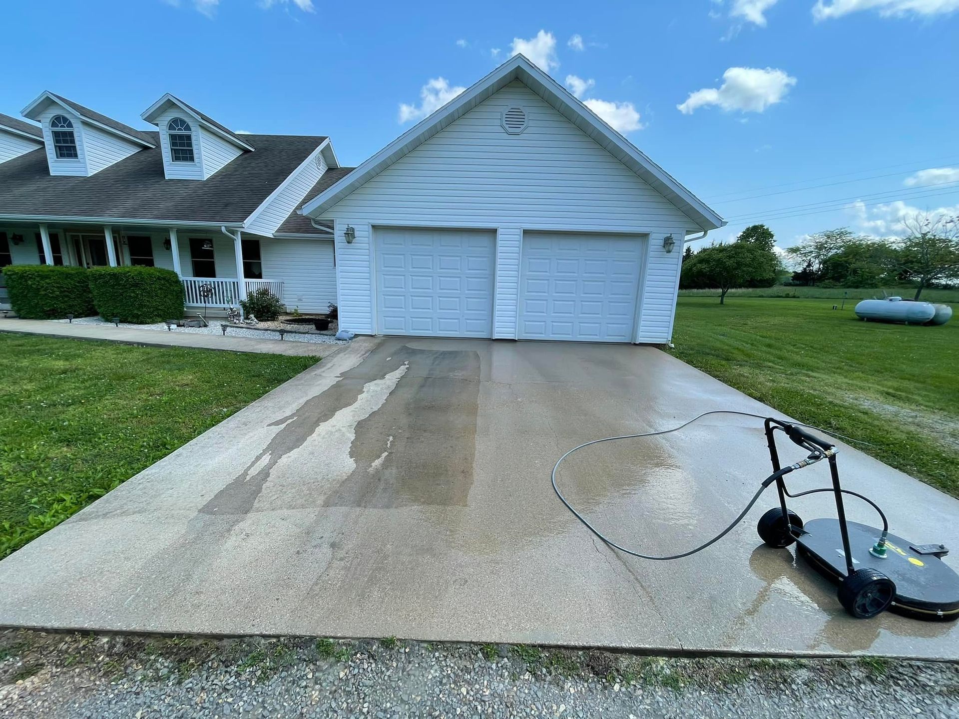 A driveway is being cleaned by a pressure washer in front of a house.