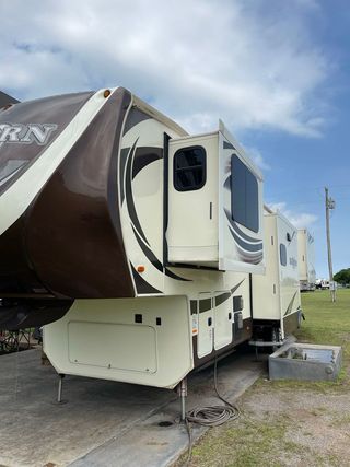 A white and brown rv is parked in a grassy field.