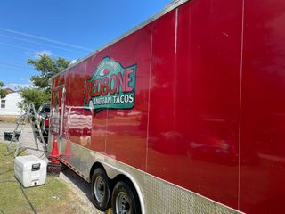 A red food truck is parked on the side of the road.