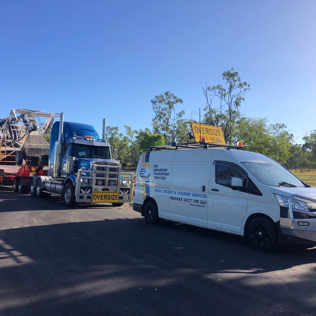 A blue semi-truck pulling a trailer and a white pilot vehicle with an 