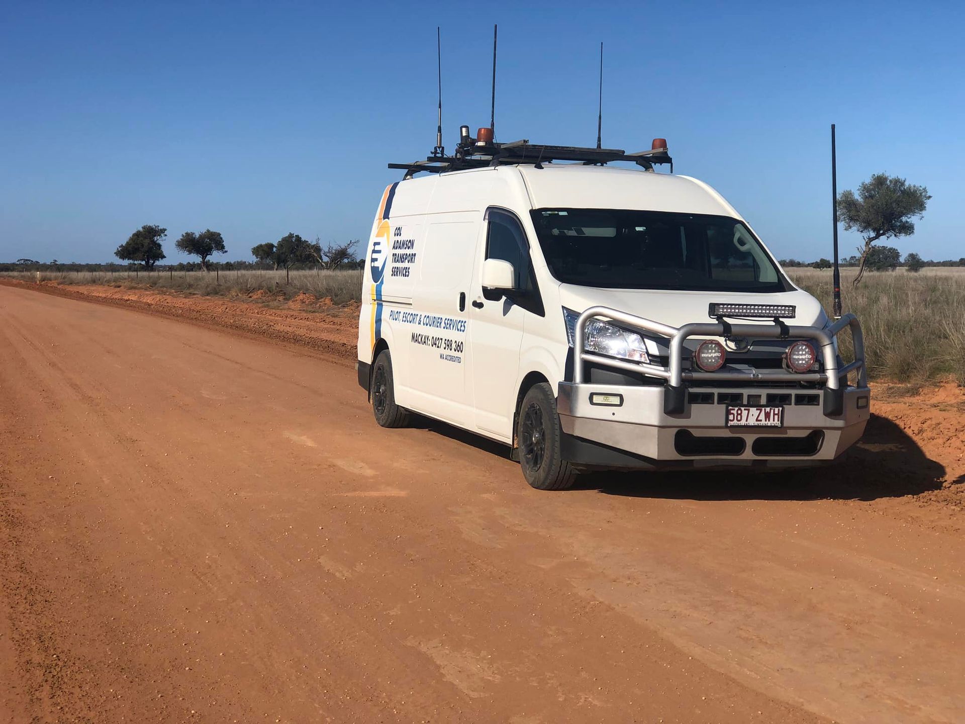 A white specialized survey van with antennas on the roof, parked on a dusty red dirt road — Col Adamson Transport Services in Farleigh, QLD
