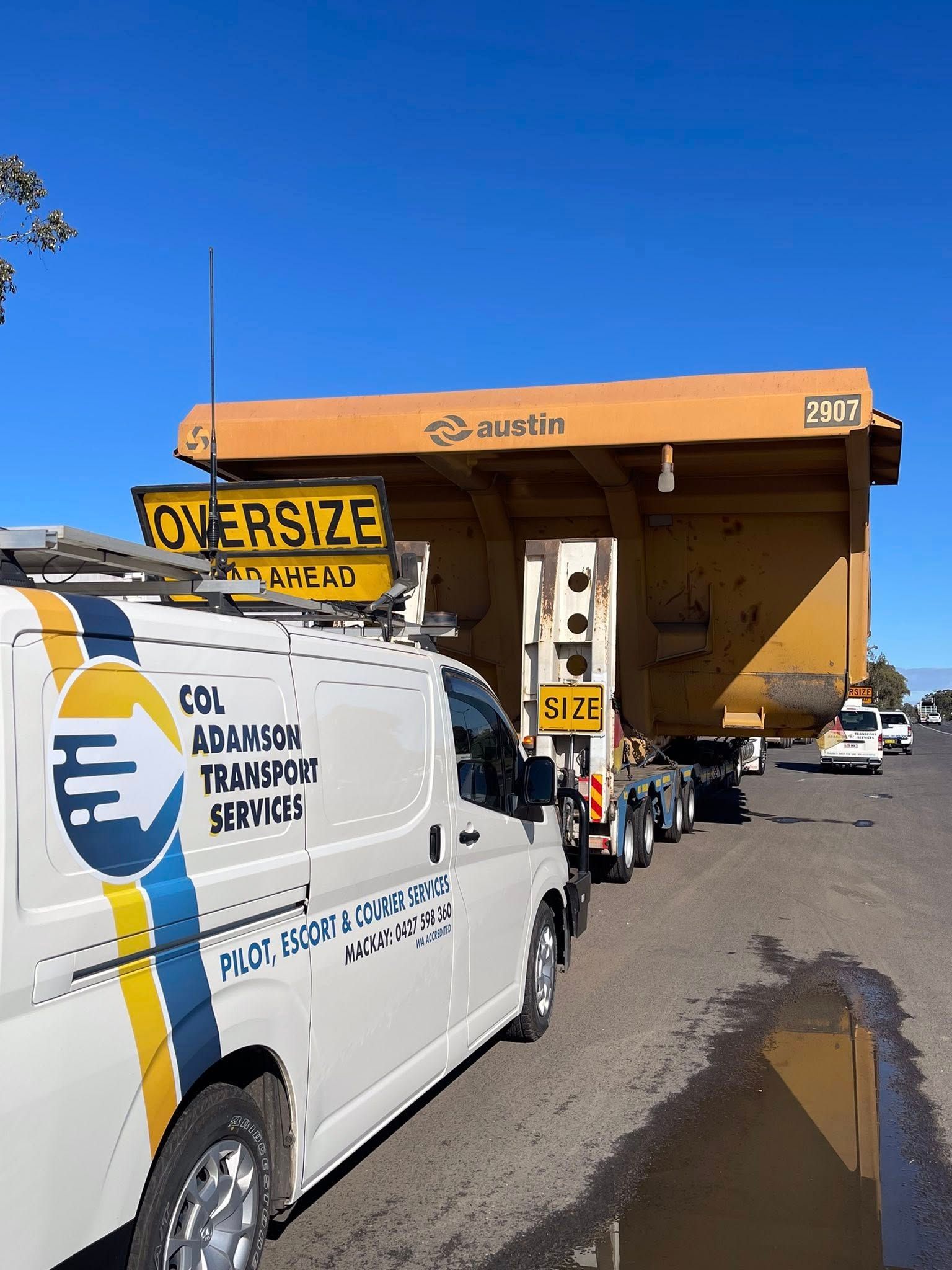 A white escort van leads a large, orange, oversized mining truck component on a road — Col Adamson Transport Services in Farleigh, QLD