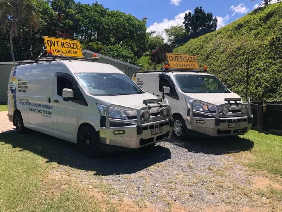 Two White Vans With Signs Parked on Gravel in Front of a Building With a Hill — Col Adamson Transport Services in Farleigh, QLD