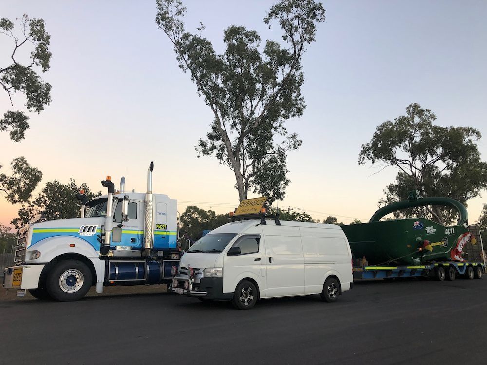 Semi-truck Hauling Large Green Object, White Van, Trees, and Dusk Sky — Col Adamson Transport Services in Townsville, QLD