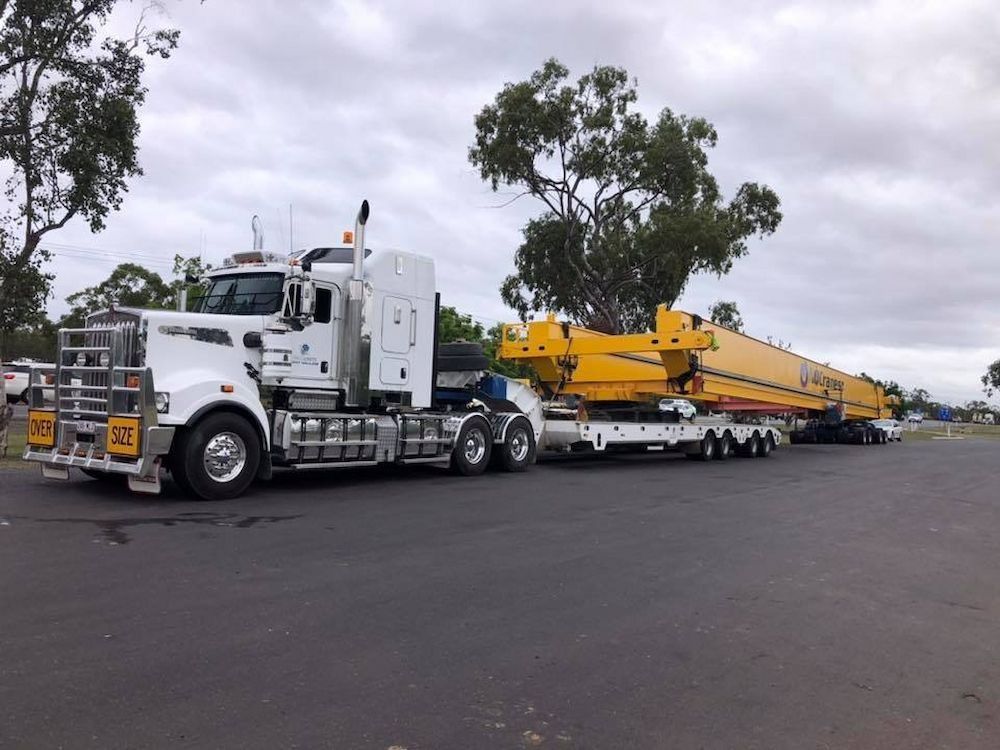 White Semi-truck Hauling Large Yellow Industrial Equipment on a Lowboy Trailer  — Col Adamson Transport Services in Townsville, QLD