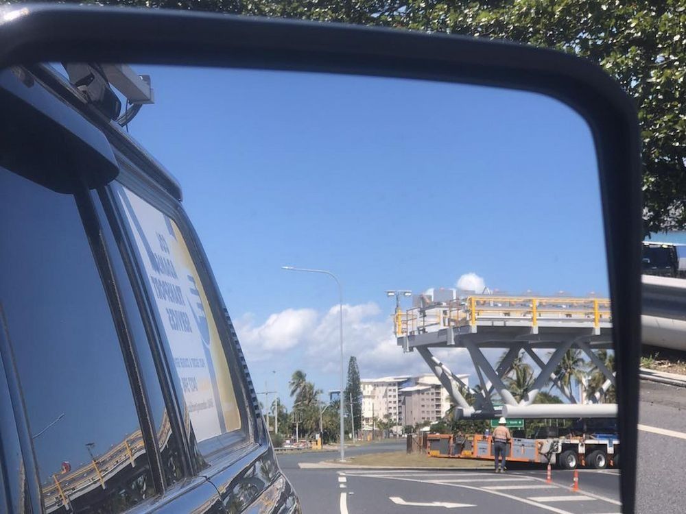 Rearview Mirror View: Large Construction Equipment on Road, Blue Sky, Buildings — Col Adamson Transport Services in Rockhampton, QLD