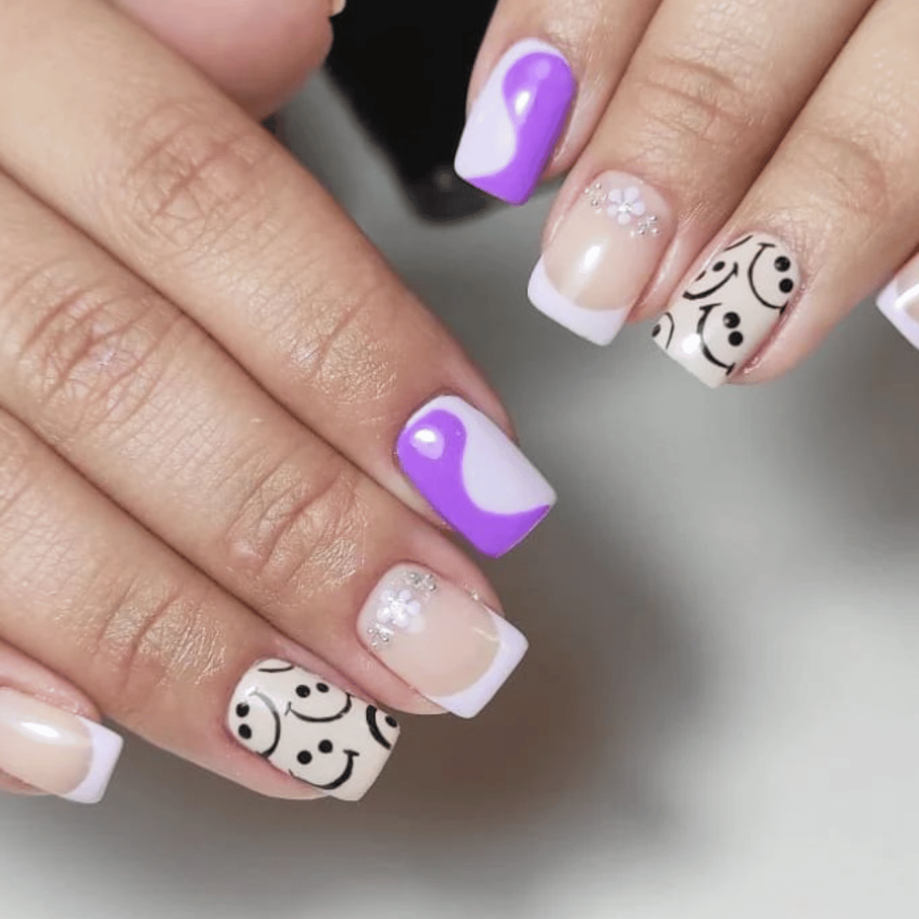 Uñas moradas y blancas con caras sonrientes.