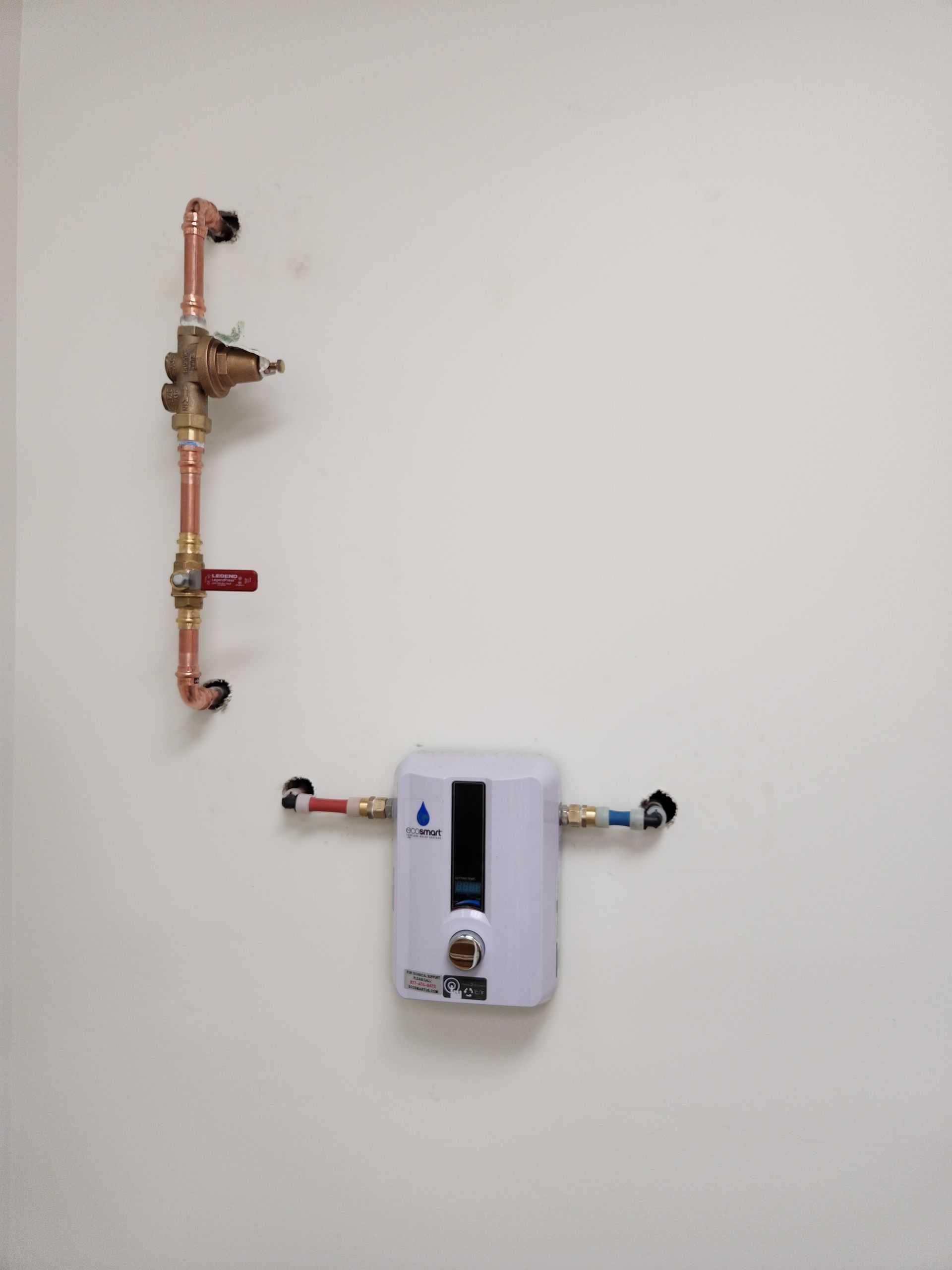 White wall with a small water heater, copper plumbing, and shut-off valve.