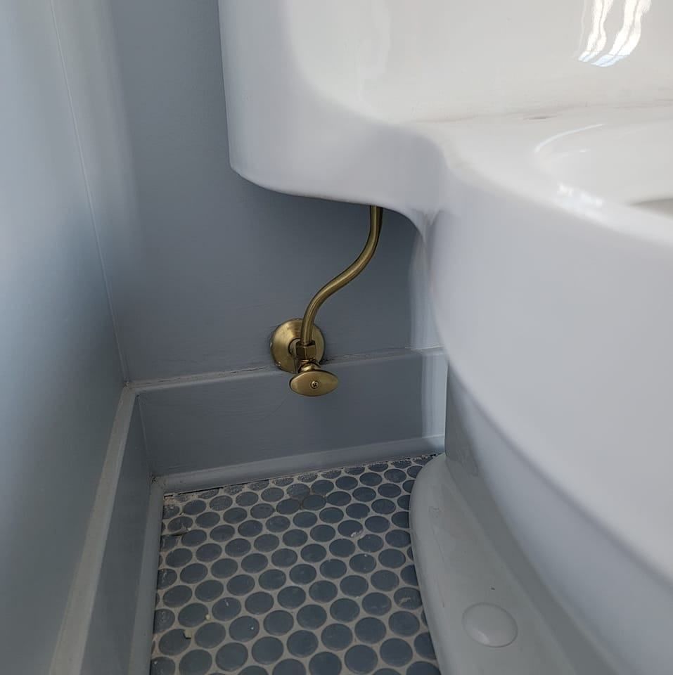 Close-up of a toilet with brass water supply components against a light blue wall, tiled floor.