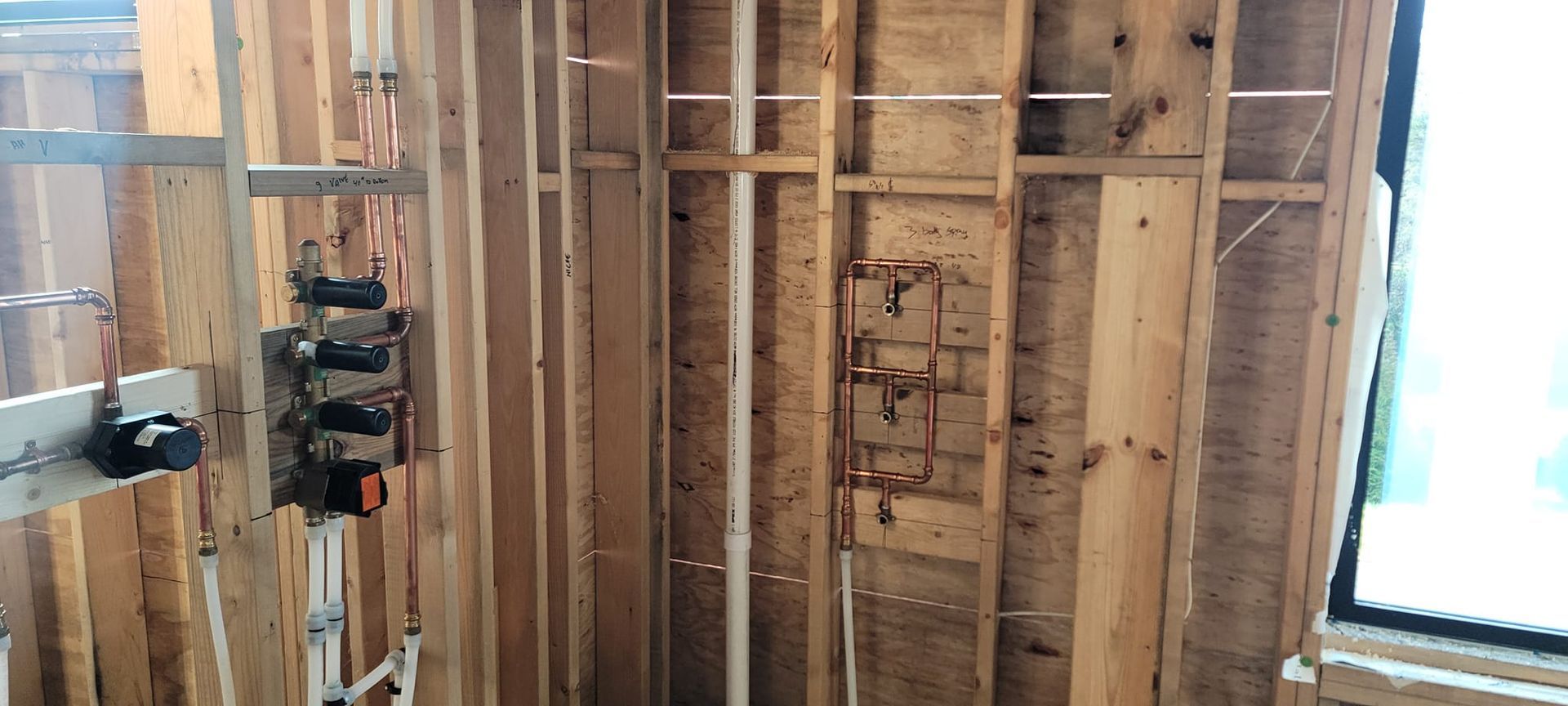Interior view of a wooden wall under construction with pipes and electrical components installed.