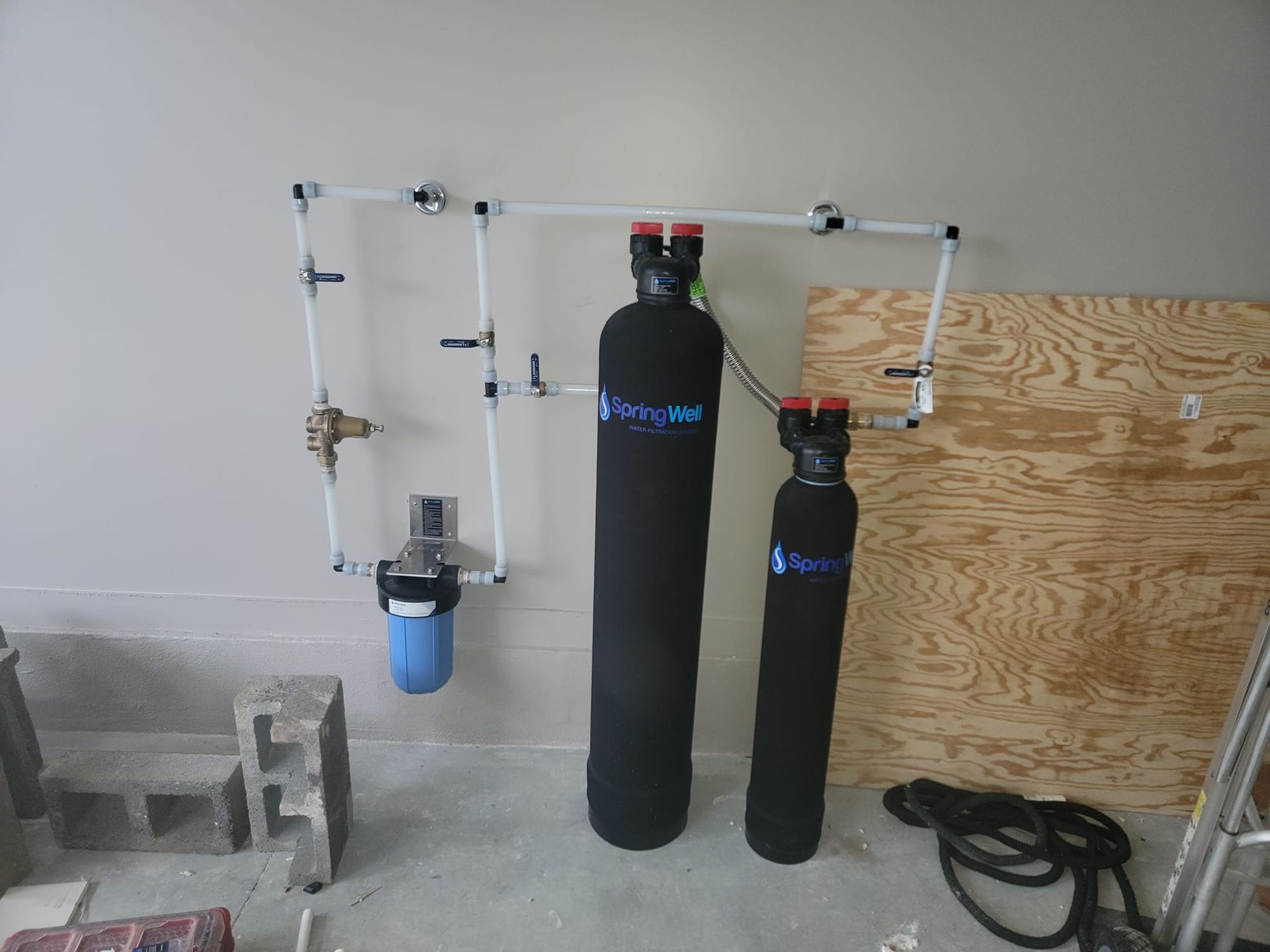 Water filtration system installed in a garage; includes multiple black tanks, white pipes, and blue filter.