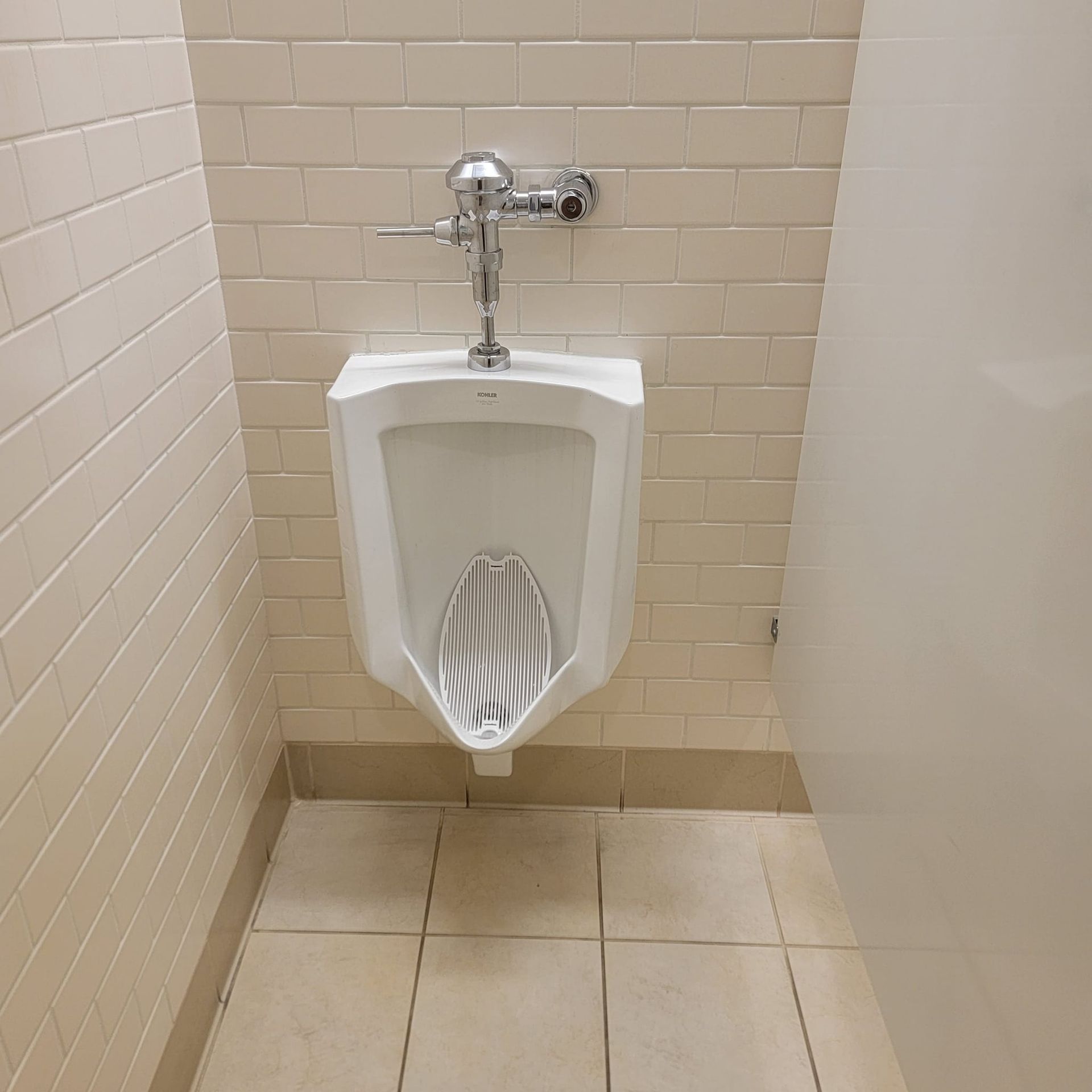 White urinal with chrome flush valve in a public restroom.