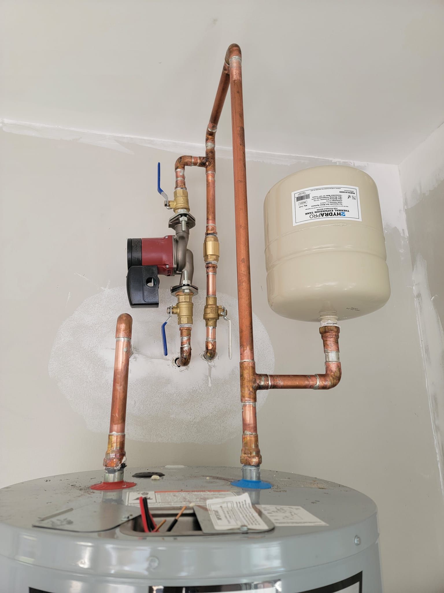 Copper plumbing connected to a water heater, with a pump and expansion tank mounted on a wall.