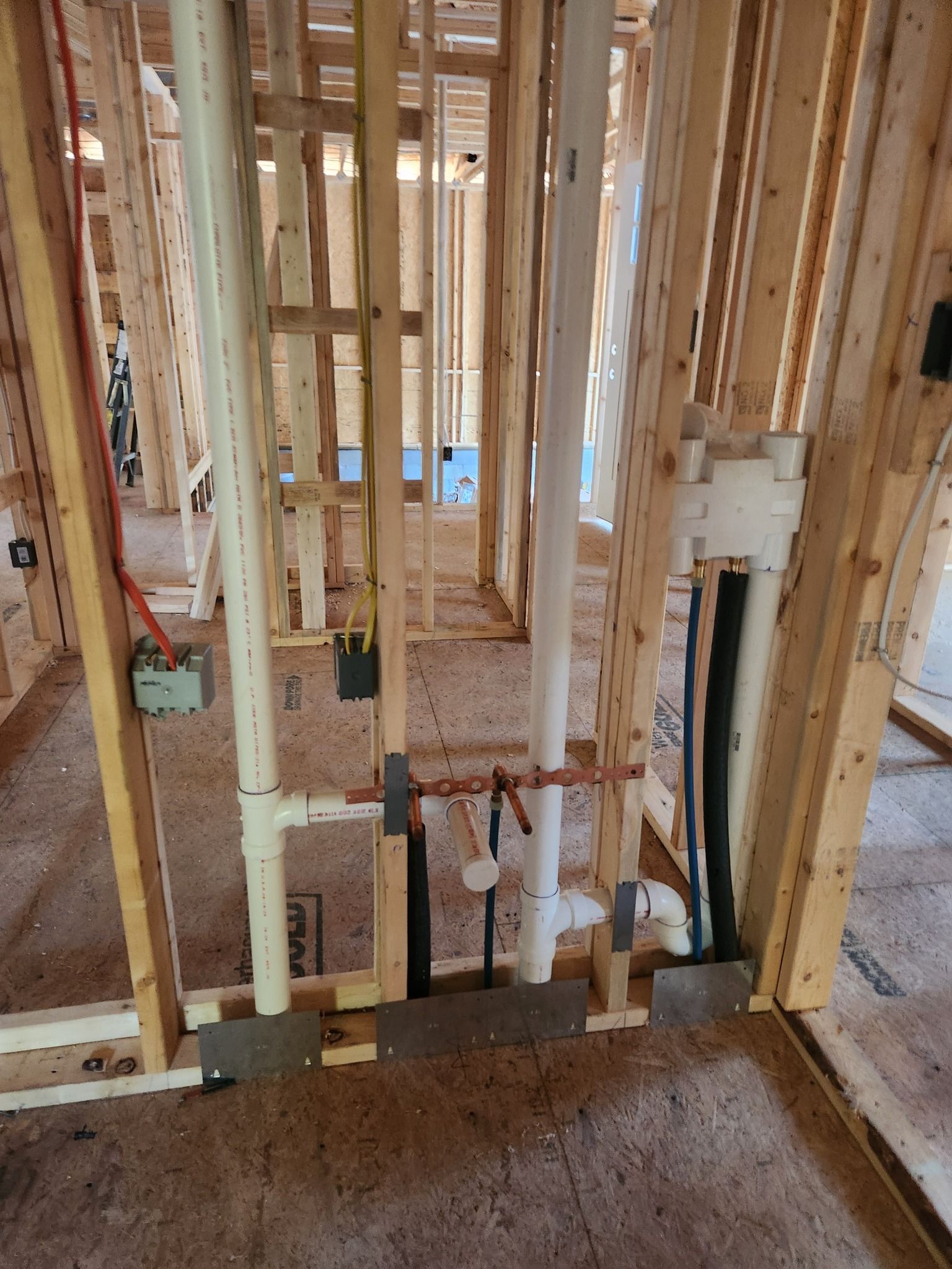Framed wooden wall with exposed plumbing and electrical wiring in a building under construction.