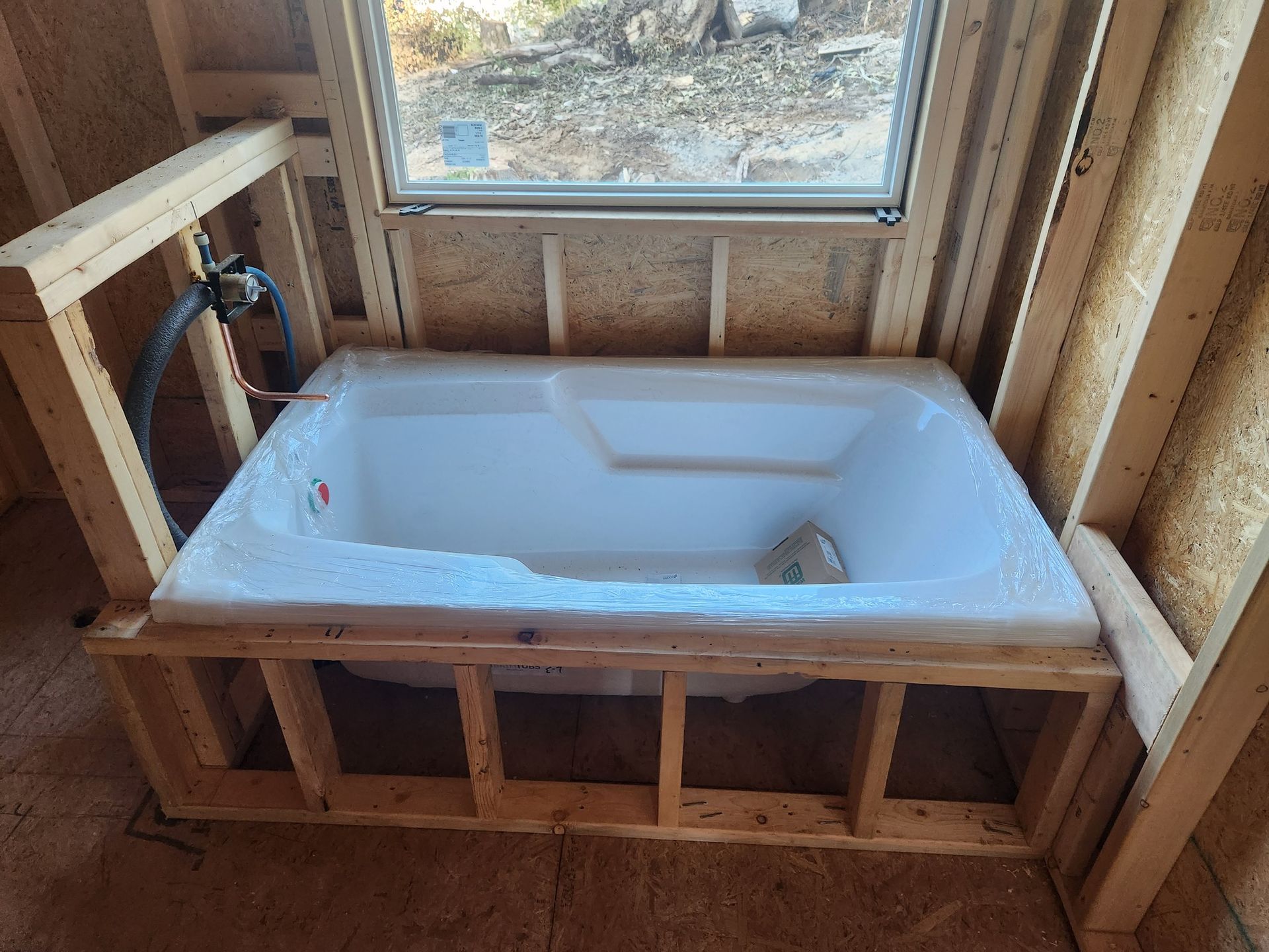 Bathtub framed in a new construction bathroom, under a window, with water lines visible.