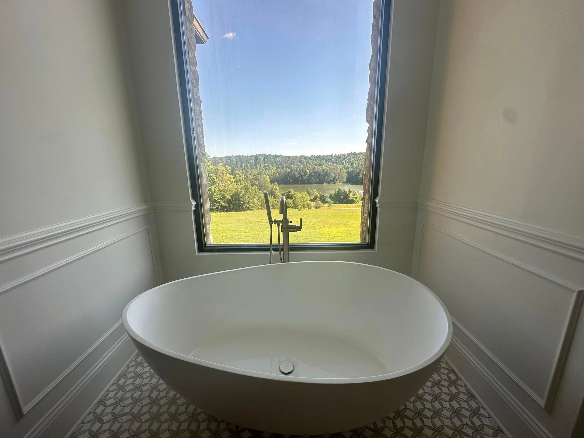 Modern white bathtub in a bathroom, with a view of a green landscape through the window.
