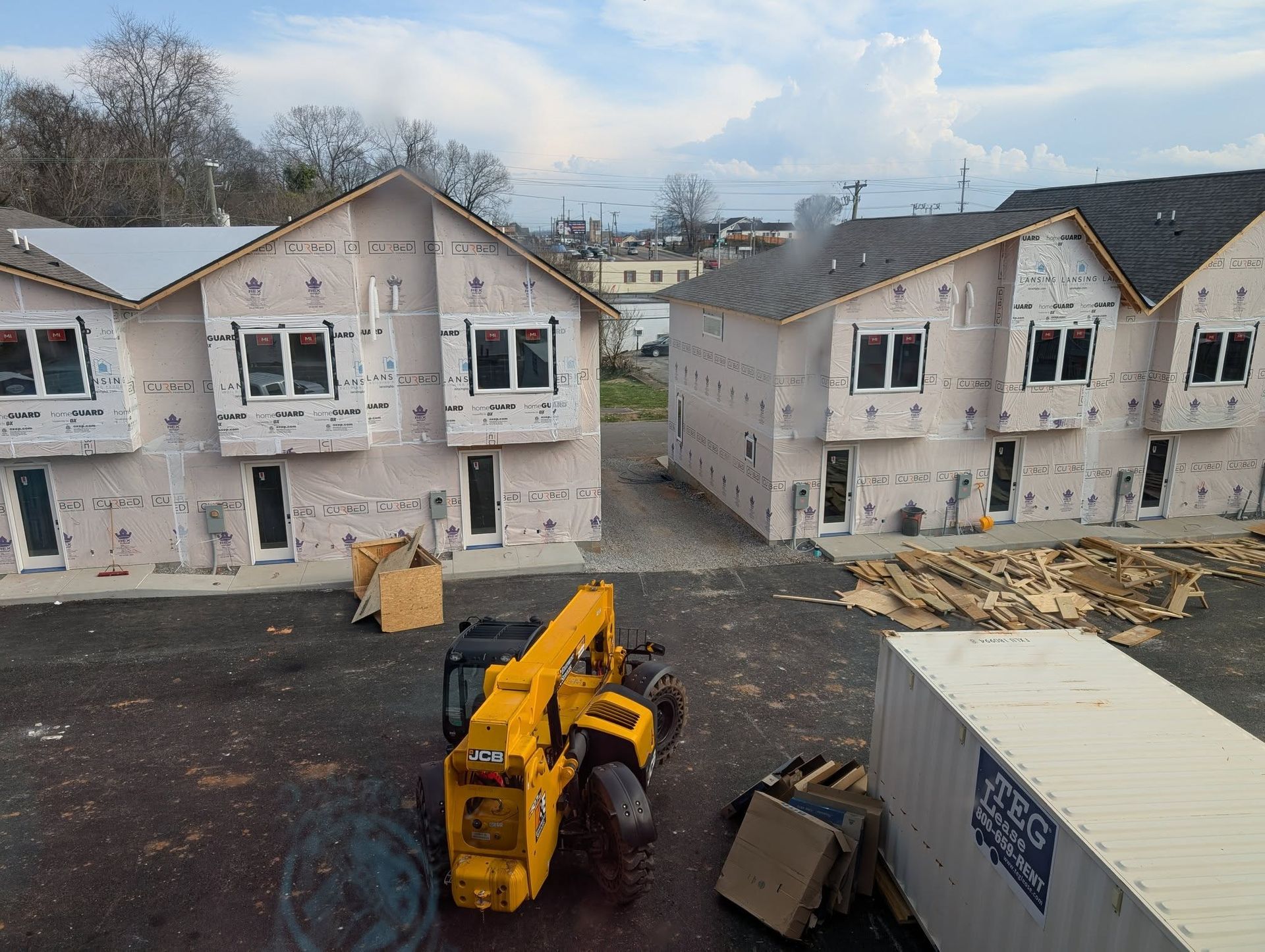 Construction site with unfinished townhouses; a yellow telehandler and a storage container are in the foreground.