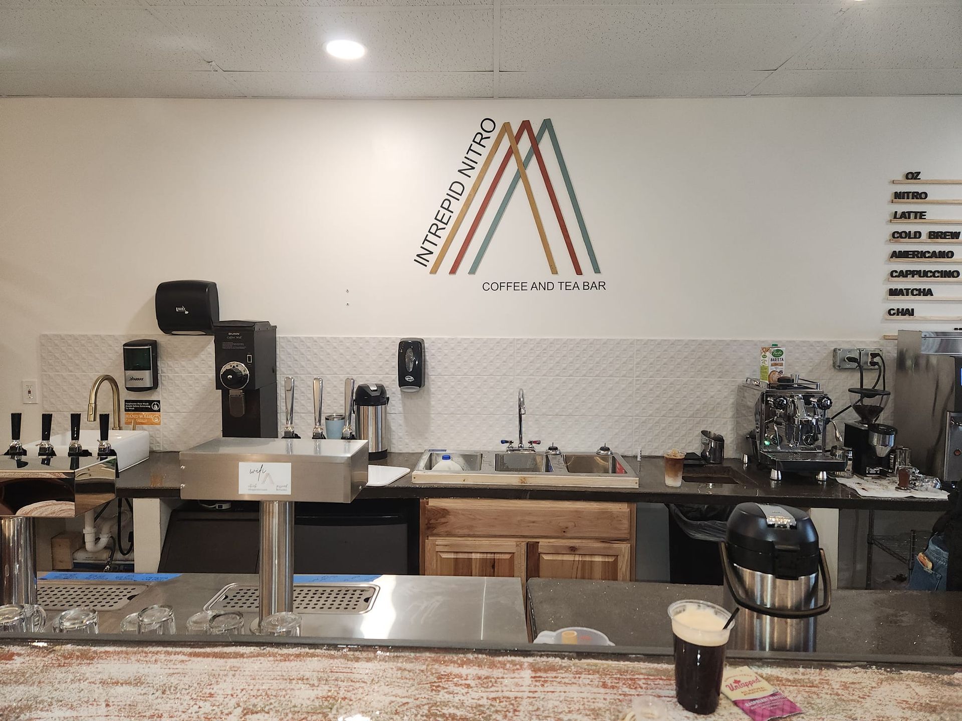 Interior of a coffee shop. Bar with equipment, a logo, and menu.