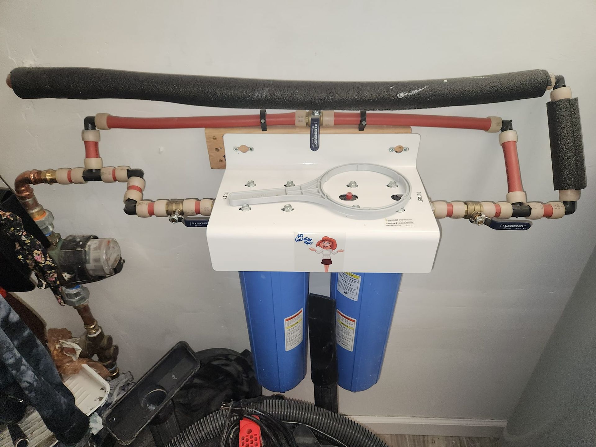 Water filtration system mounted on a wall with blue filter housings and connected pipes.