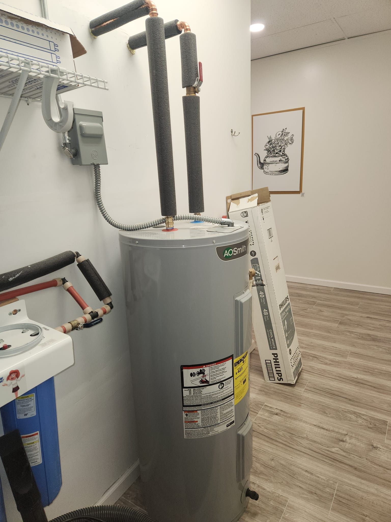 A gray water heater with black insulated pipes and a nearby water filtration system in a room.