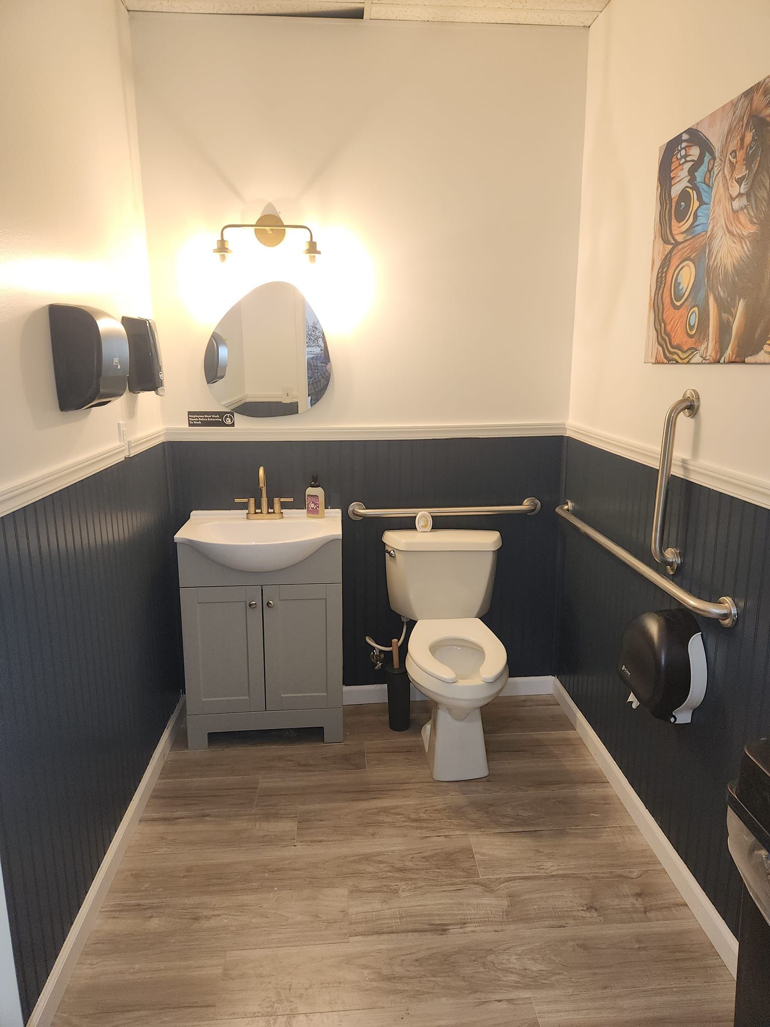 Accessible restroom with a toilet, sink, and hand dryer. Features grab bars and an art piece.