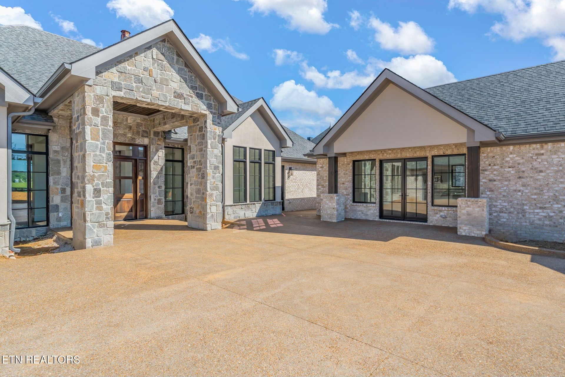 Stone facade home with gray roof, windows, and tan gravel driveway.