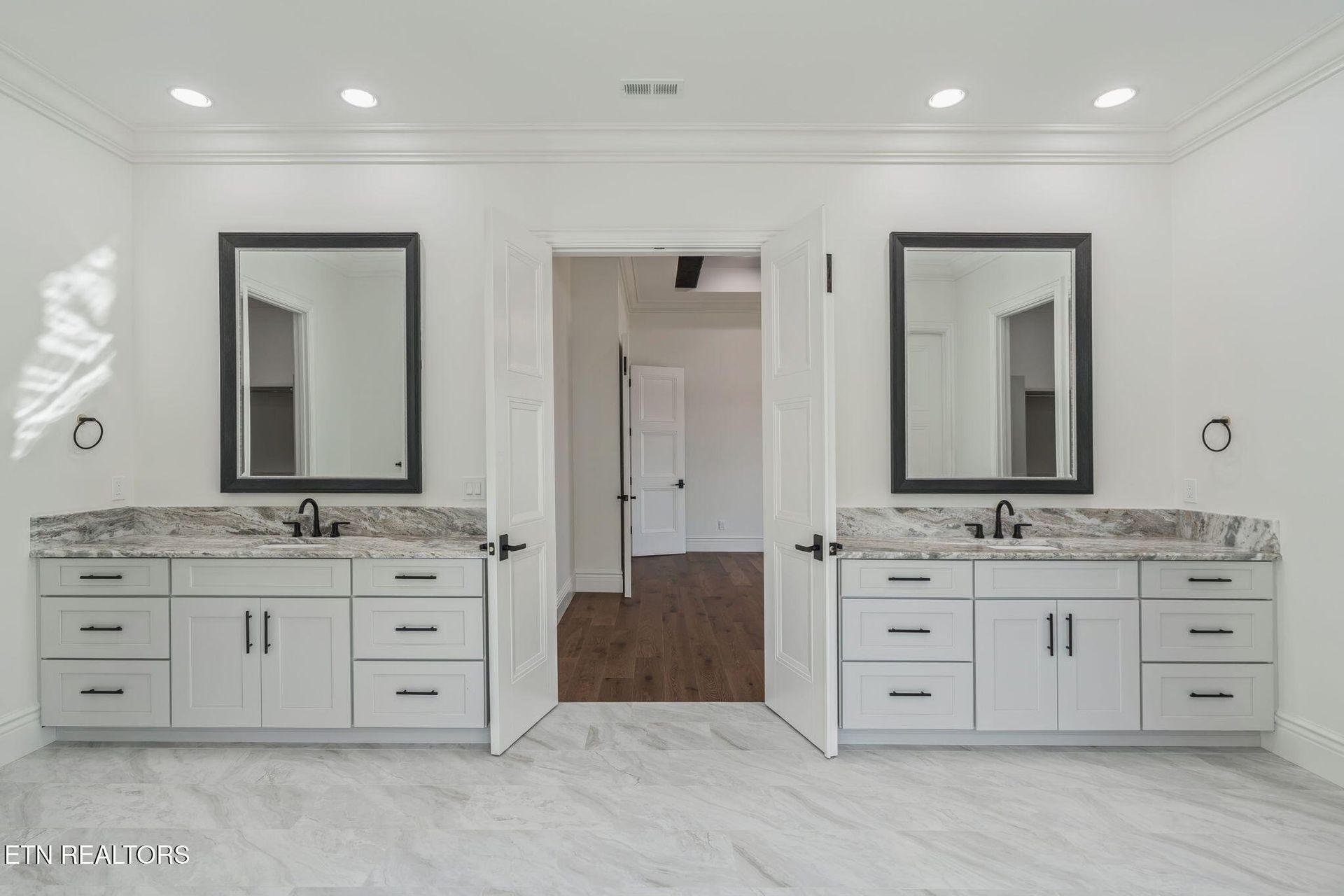 Bathroom with two white vanities, each with a dark-framed mirror and granite countertop, facing each other.