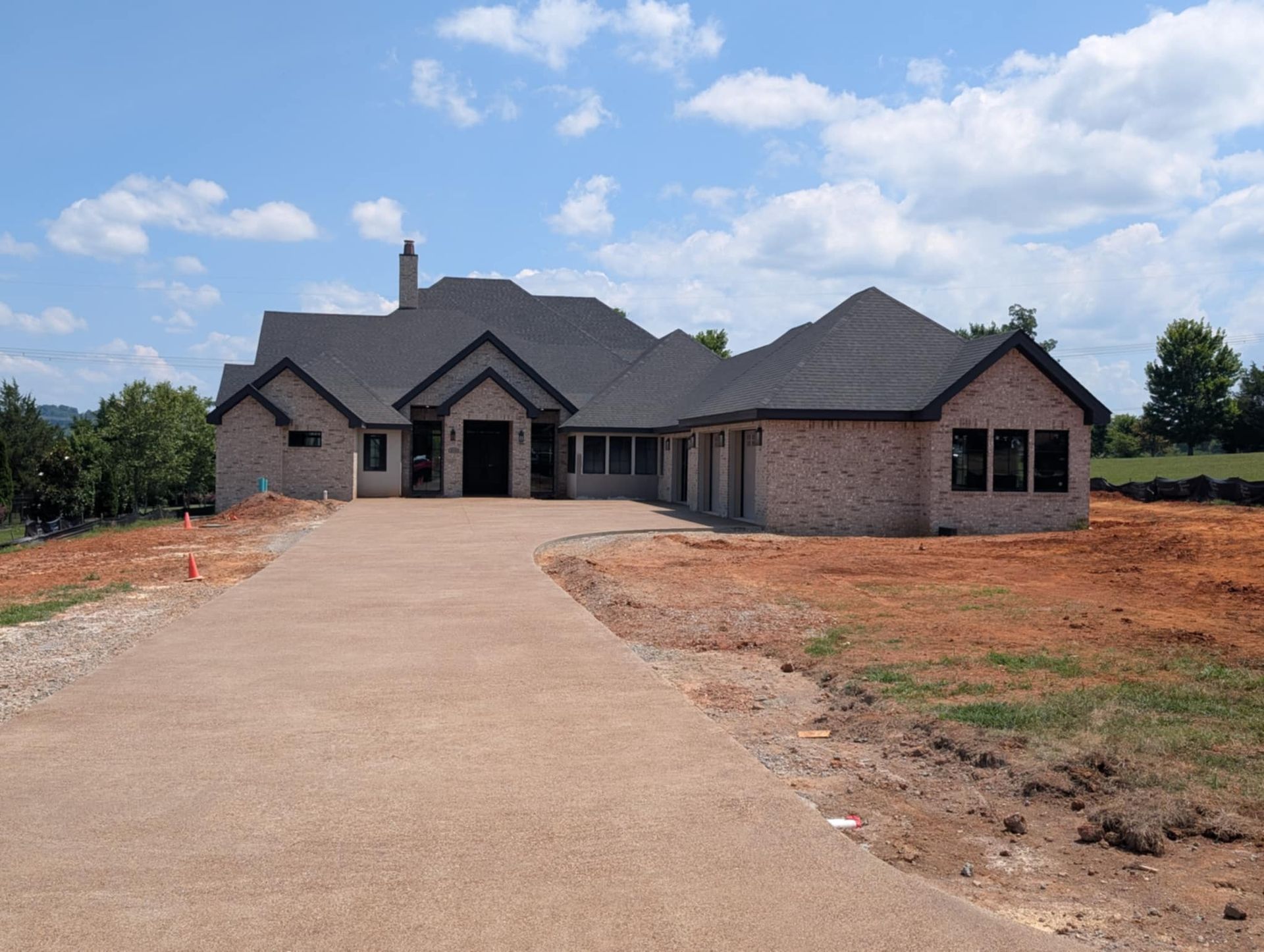 New brick house under construction, with a long driveway and clear sky.