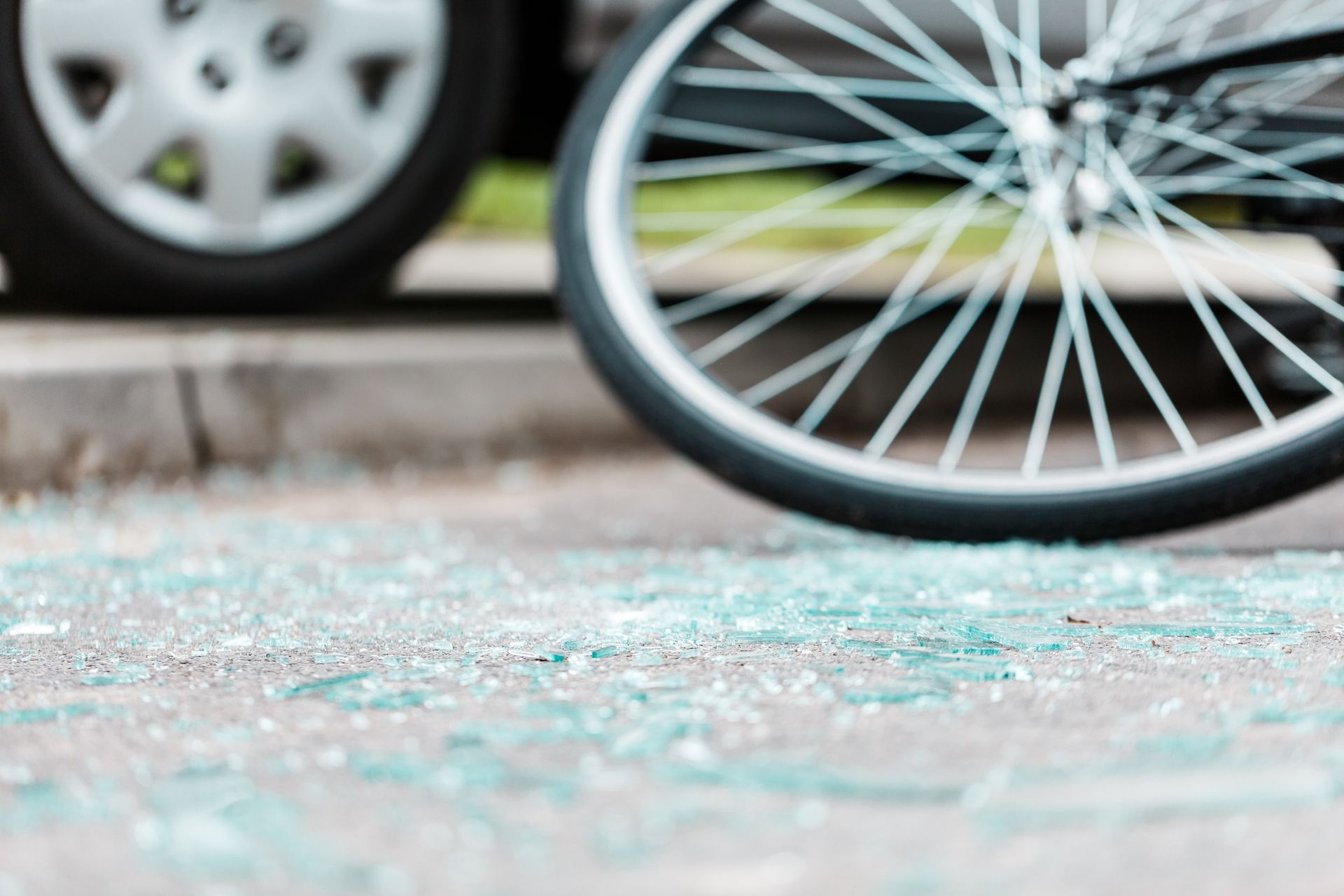 Shattered glass on pavement near a car tire and a bicycle wheel, suggesting a collision.