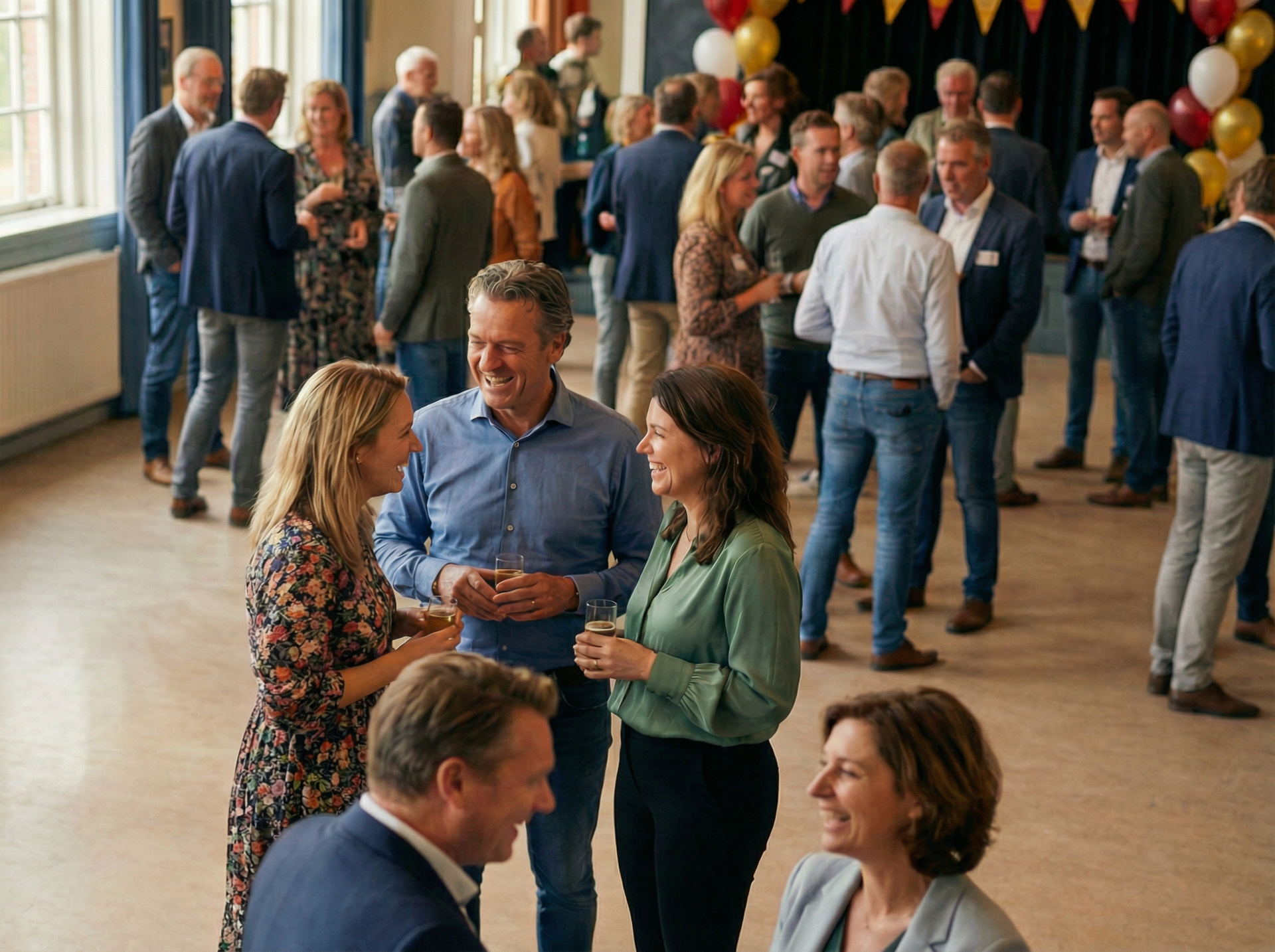 Een groep mensen is bijeen in een goed verlichte ruimte met eten en drinken. Mensen praten met elkaar en omhelzen elkaar.