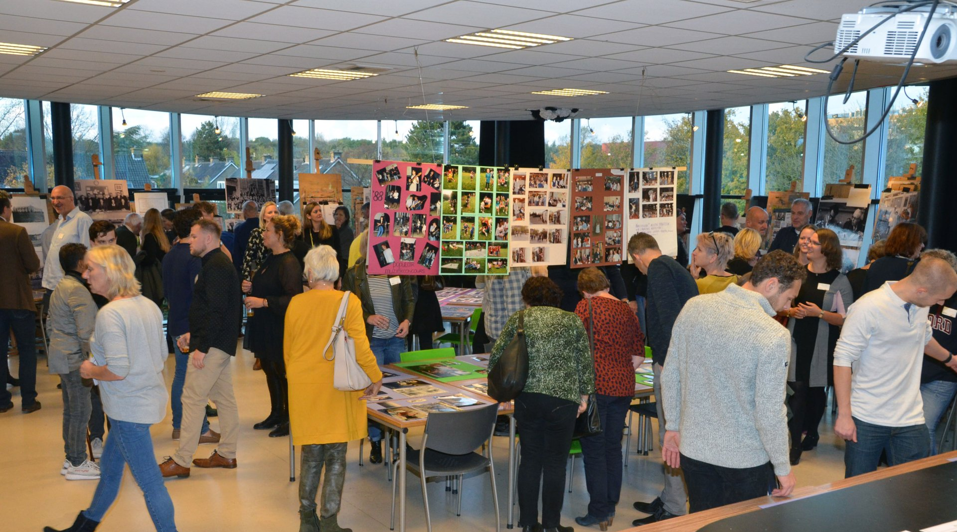 Mensen op een evenement bekijken foto's die op kleurrijke borden in een lichte zaal worden tentoongesteld.